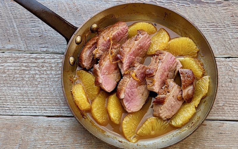 Duck a l'Orange in a copper frying pan on whitewashed background