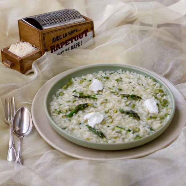 Asparagus and Goat Cheese Risotto Asparagus and Goat Cheese Risotto in green flat bowl on a sheer cloth with silver cutlery and wooden box grater (Zero Food Waste)