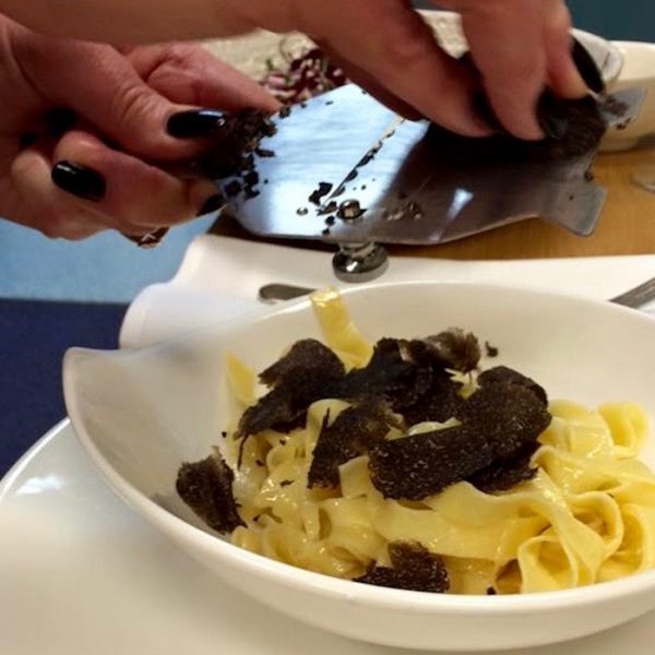 Hand using stainless steel truffle grater to grate a black truffle over a white bowl of fettucine pasta (Truffle Recipes)
